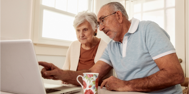 An elderly couple is looking at a laptop while the man is pointing at the screen. 