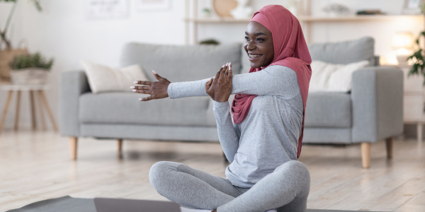 A woman wearing a burka stretching on a yoga mat in front of a laptop on the floor.