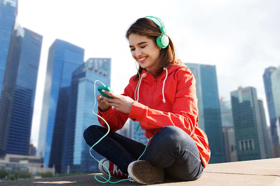 Woman with earphones sitting on sidewalk