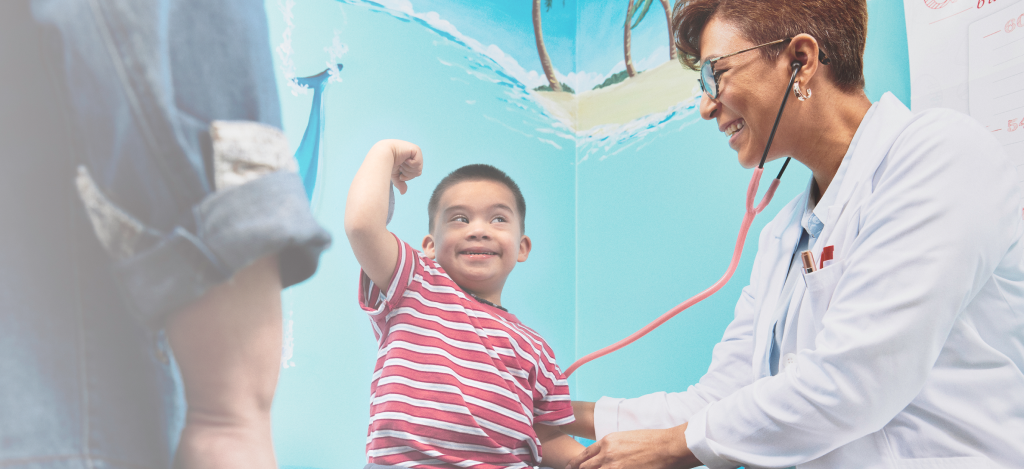 A doctor with a stethoscope is smiling and examining a smiling young boy in a striped shirt.
